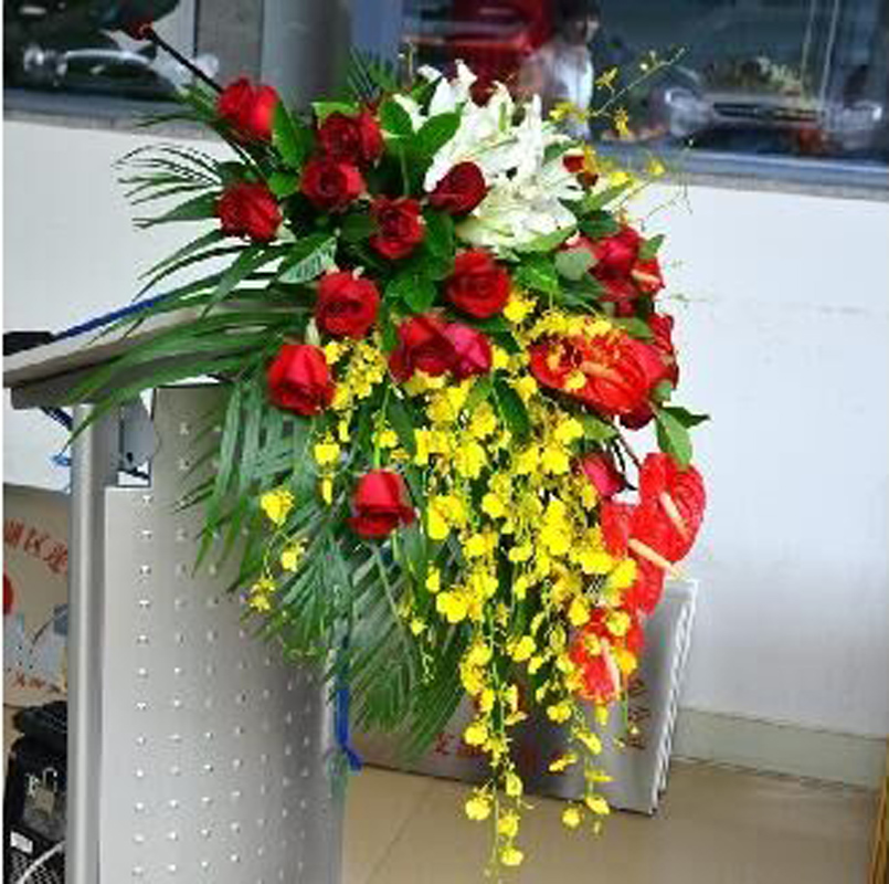 讲台花4   20支红玫瑰，10支跳舞兰，5朵白百合，5支红掌，其他绿色叶材及散尾葵适量 长度约60-70cm(1406)